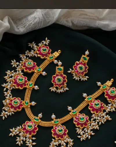 A floral kundan necklace and earrings with pearl sprays on green cloth.