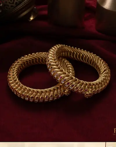 A pair of twisted gold kadas set with rubies on maroon cloth.
