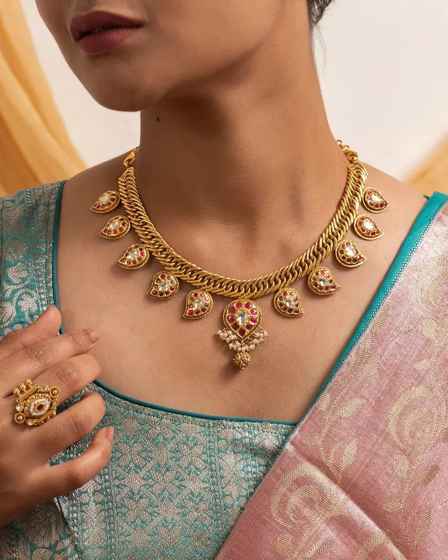 A gold necklace with red stone drops worn over a teal silk saree.